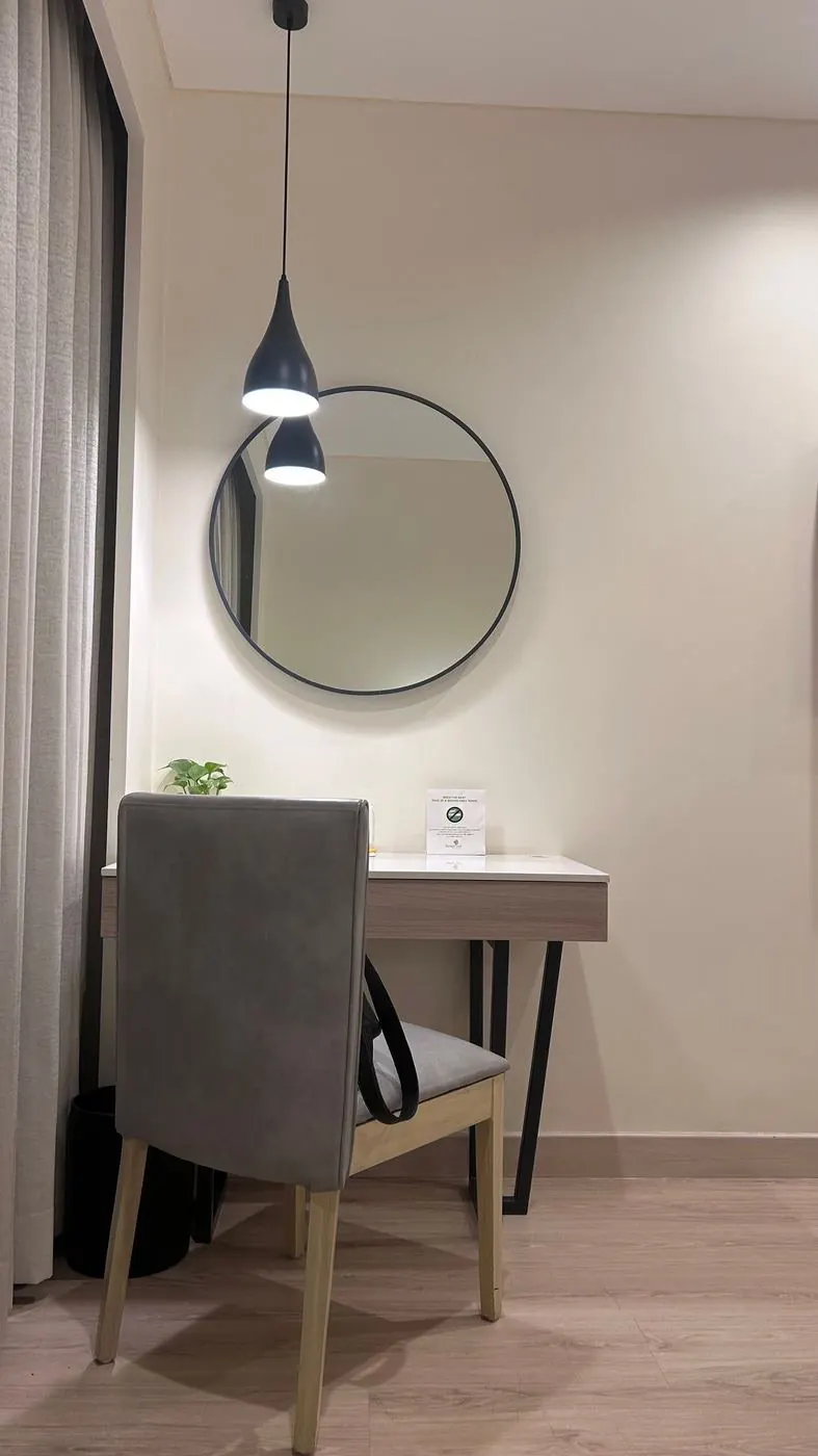Home office nook with a cream wall, round mirror, desk and grey chair, before any AI edit